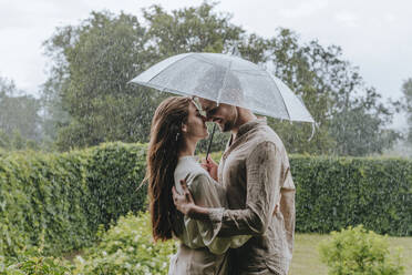 romantic couple standing with umbrella in rain at garden