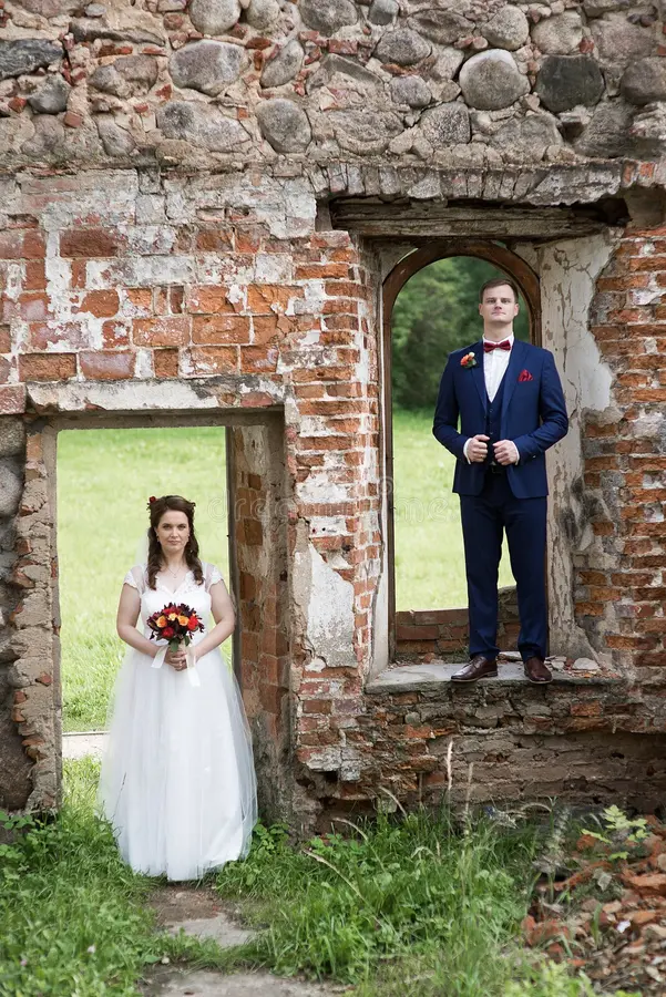 young wedding couple framed old brick bride groom pose separate window frames grass soft light behind them forming 421895477